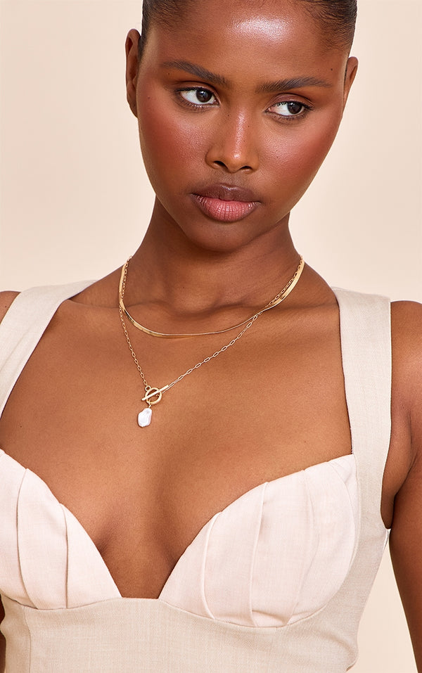 https://cdn-img.prettylittlething.com/1/d/c/9/1dc9d56dc4ec2576a5df0ece789a4619af704f65_CNN3217_1_gold_layered_t_bar_necklace_with_pearl_detail.jpg